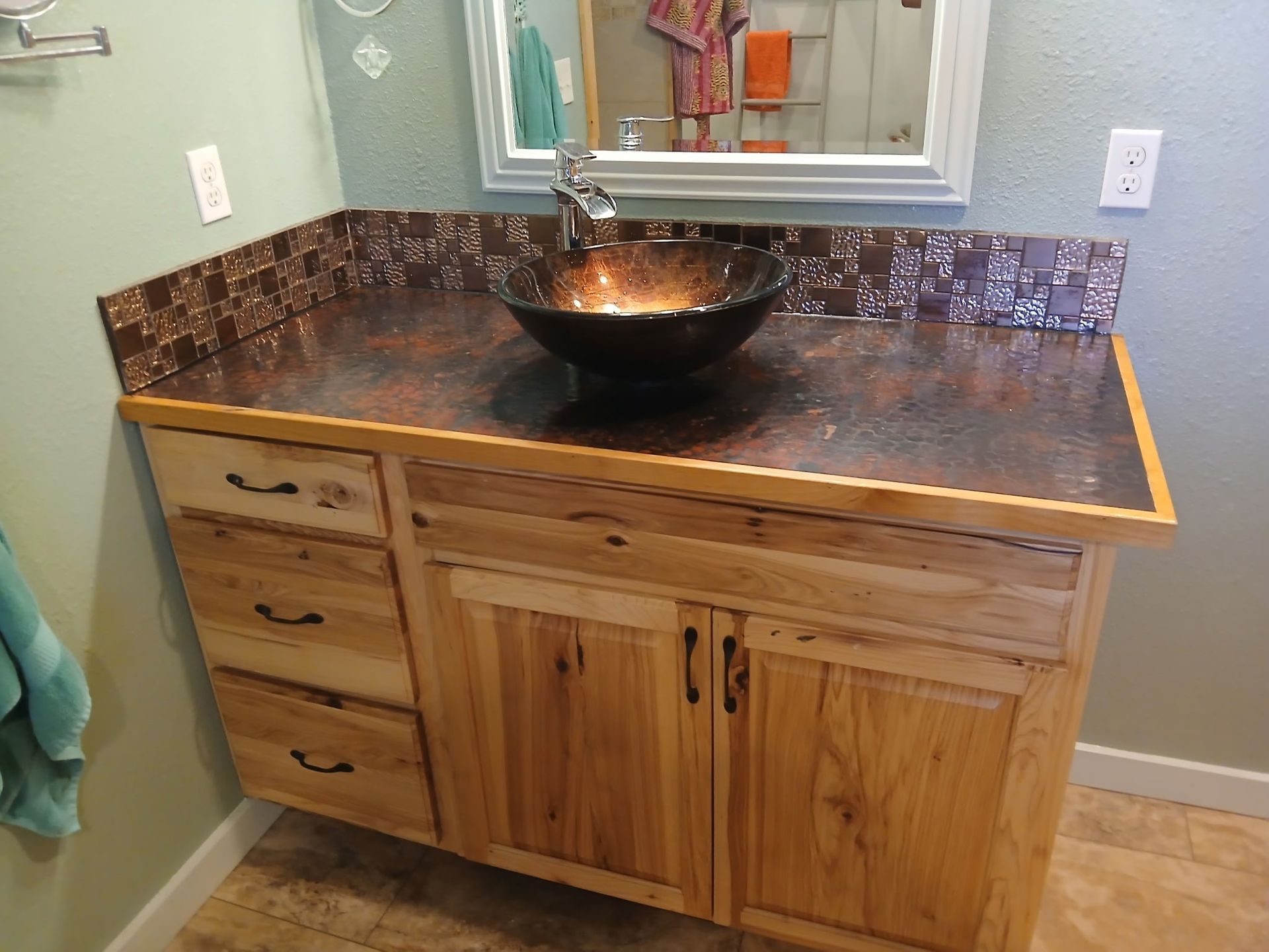 Rustic wooden bathroom vanity with copper countertop, bowl sink, and backsplash; green walls.