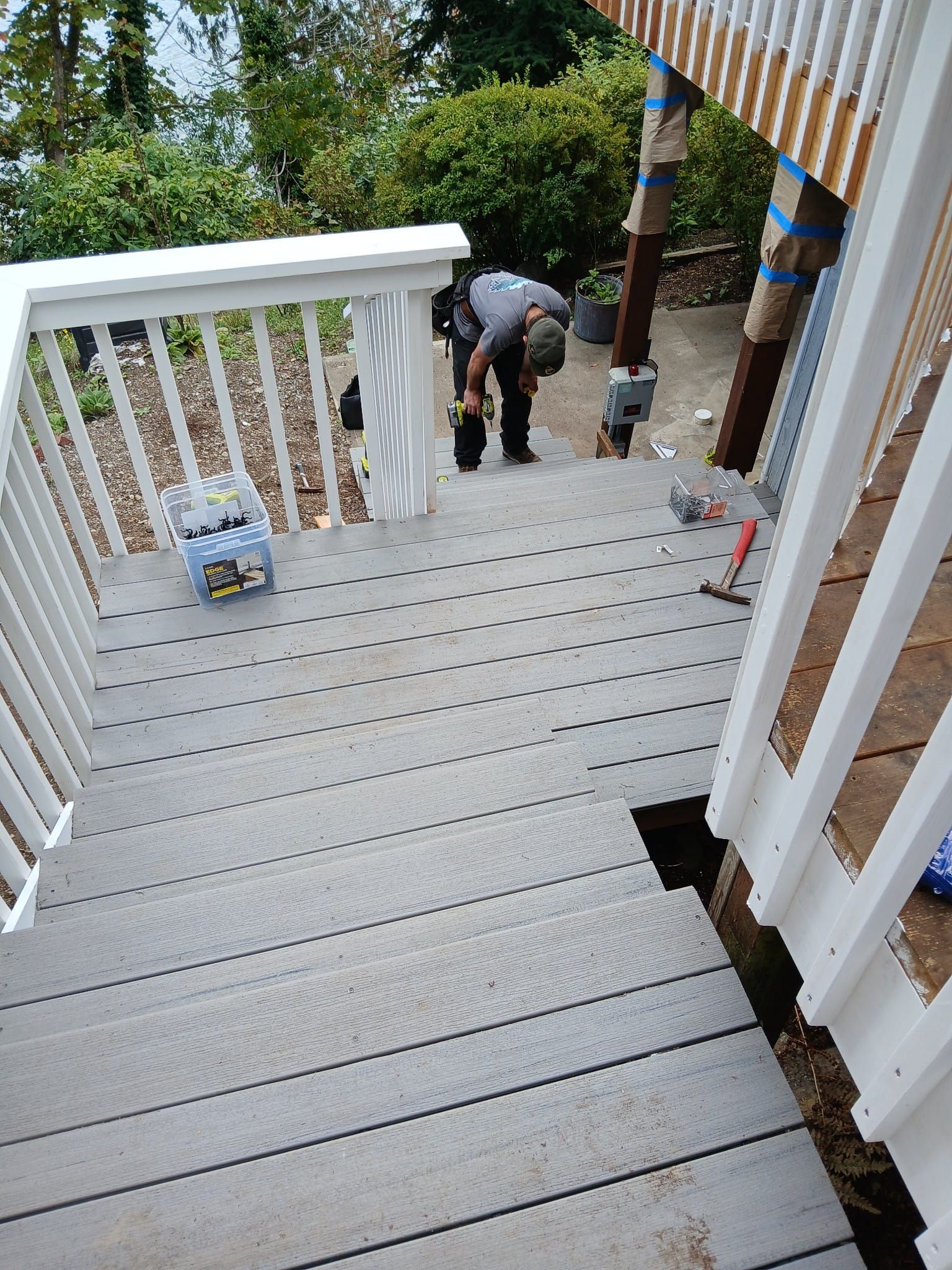 Person working on a grey deck with white railings. Bottles of water sit nearby.