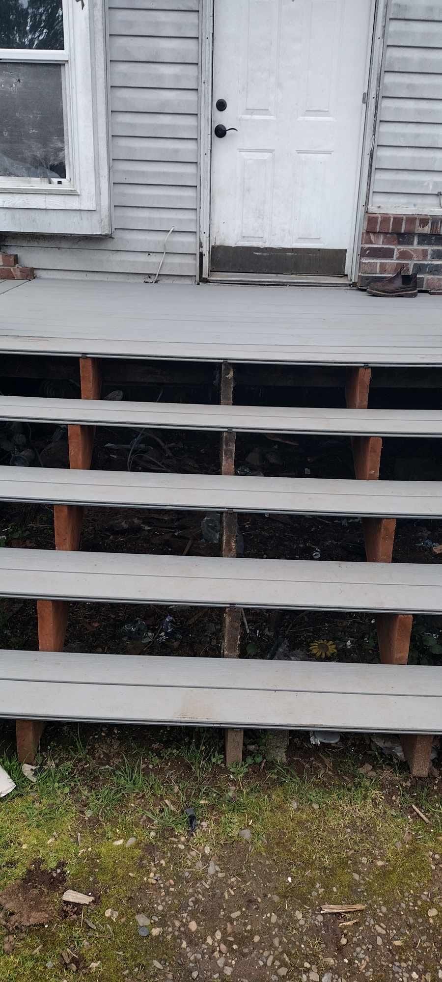 Dilapidated house with gray wooden steps leading to a white door.