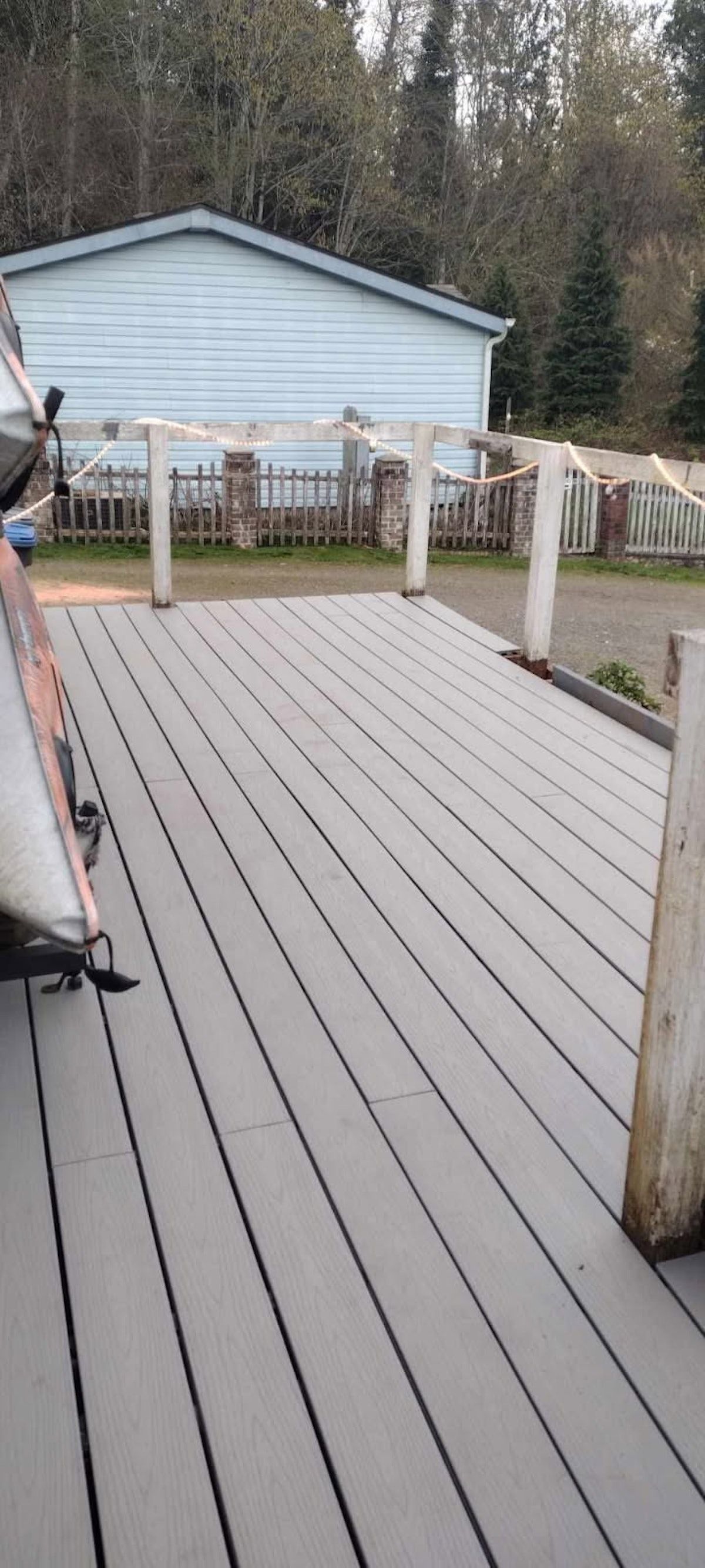 View of a gray deck with a blue building and trees in the background.