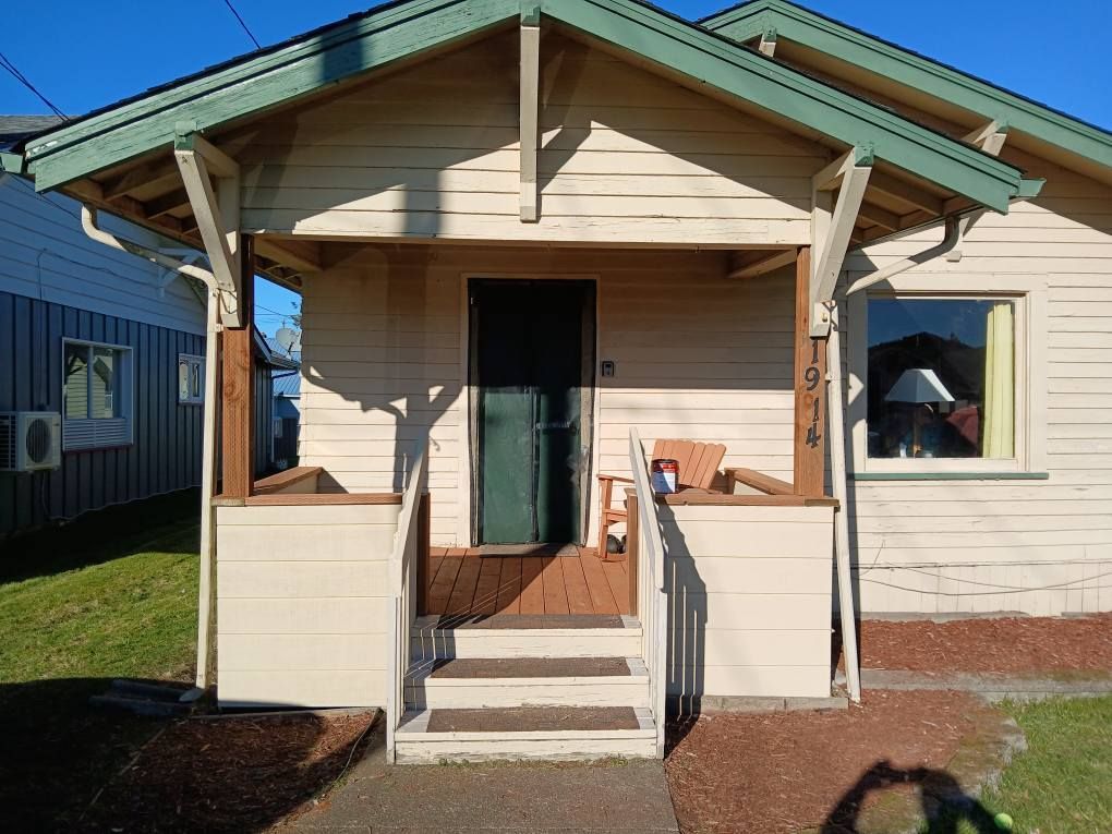 A small, light-colored house with a porch and steps; a green door is centered under the roof.