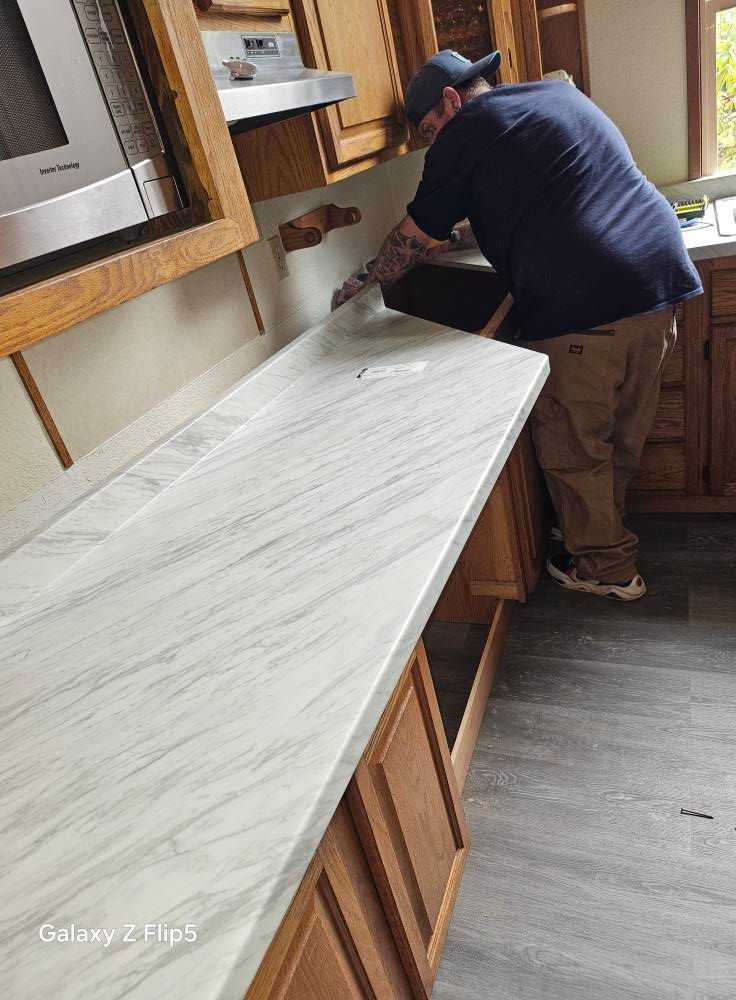 Man installing a light grey marbled countertop in a kitchen with wooden cabinets.