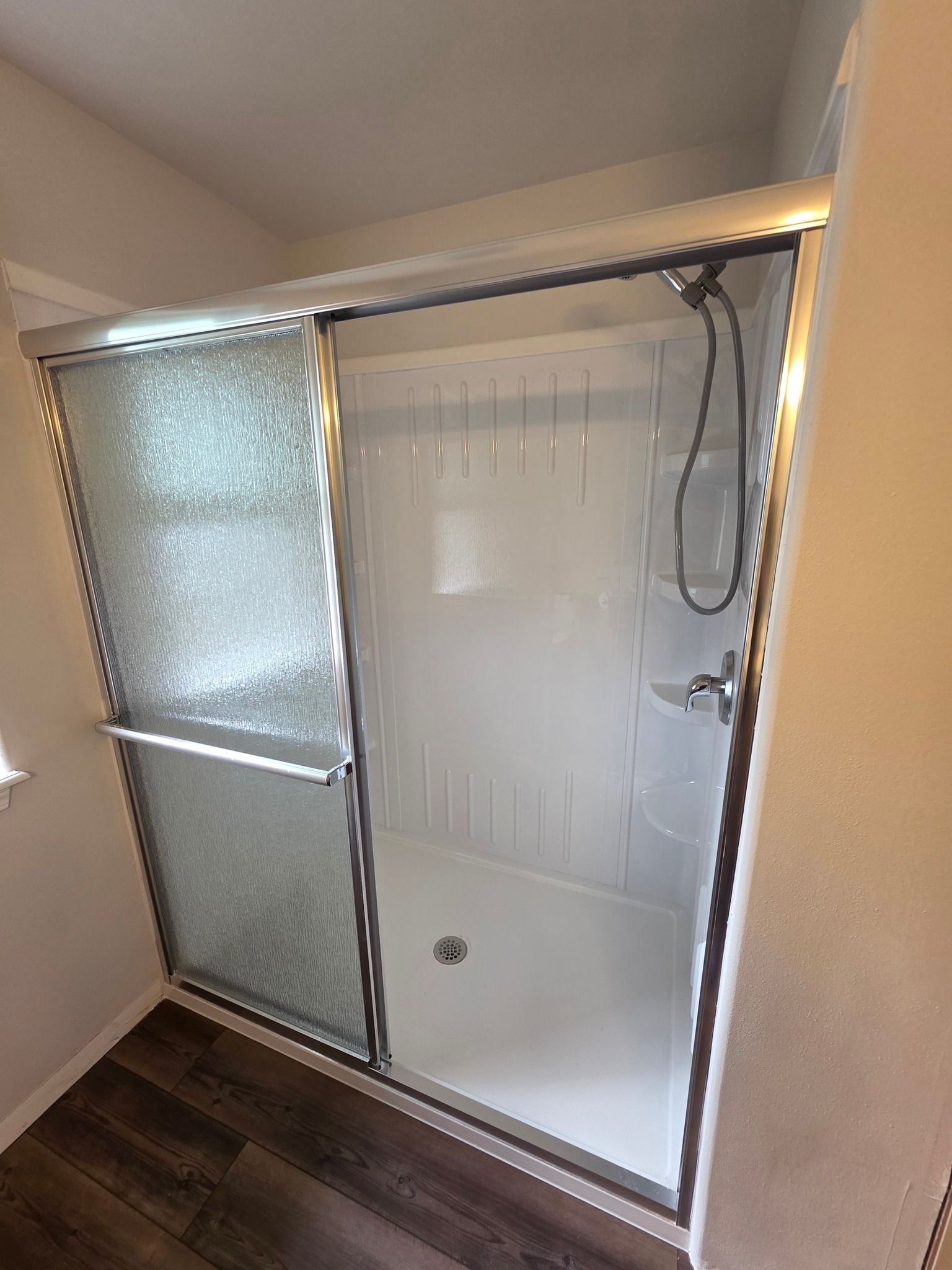 A white, pre-fab shower with sliding frosted glass doors and a chrome showerhead in a bathroom.