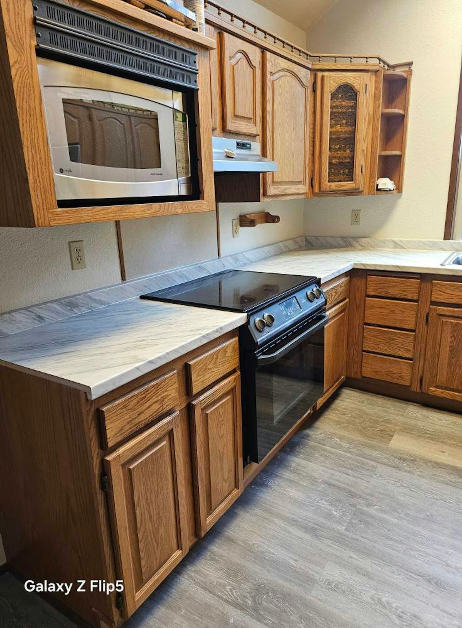 Wooden kitchen with microwave, stove, cabinets, and light countertops.