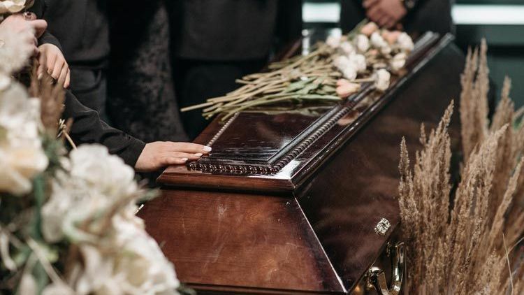 Family members paying their respects at a funeral service, with flowers placed on a wooden casket