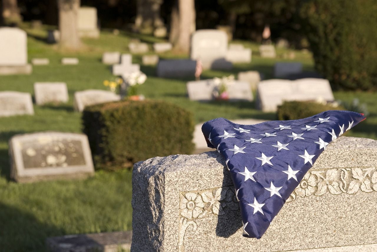 An American flag folded on a gravestone in a peaceful cemetery with headstones in the background.