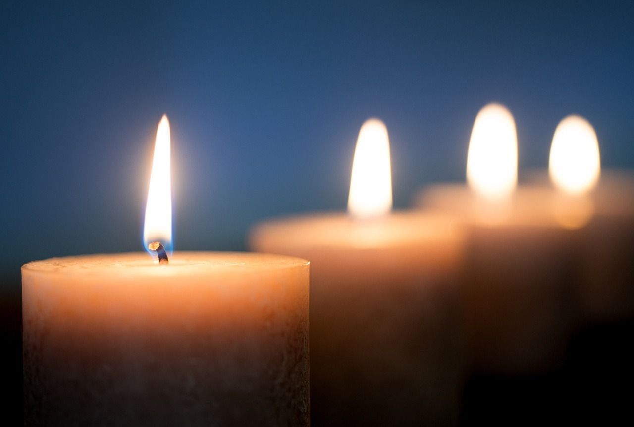 Close-up of a lit candle with a warm, glowing flame, against a blurred background of other candles.