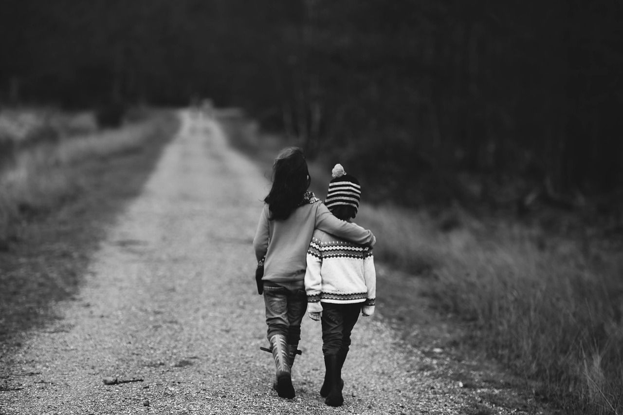 Two kids walking while hugging, on a dirt road