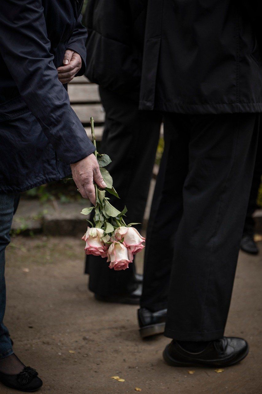 Several men in a line, all wearing suit, one holding a bouquet of pink roses