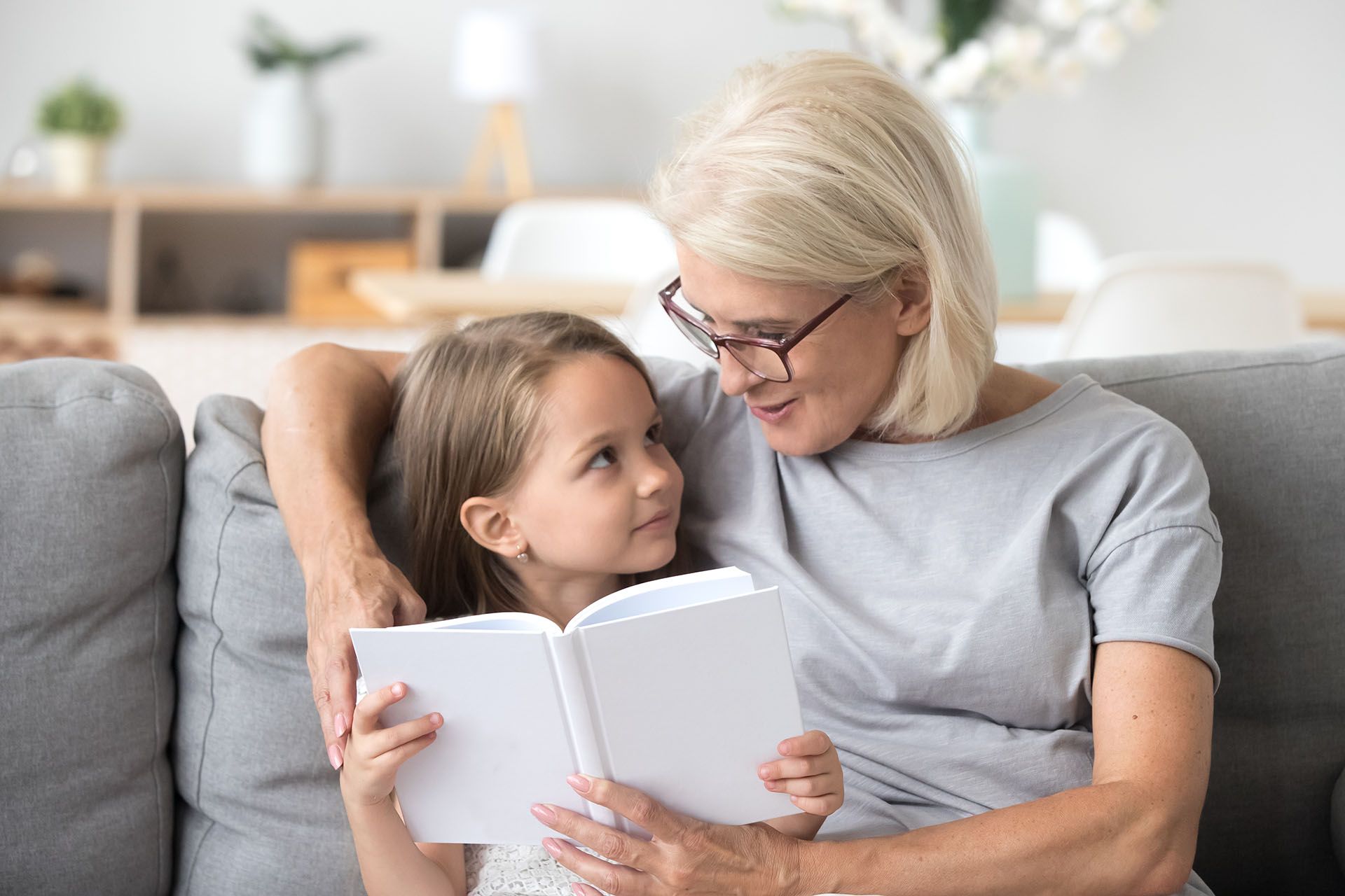 A woman and a little girl are sitting on a couch reading a book.