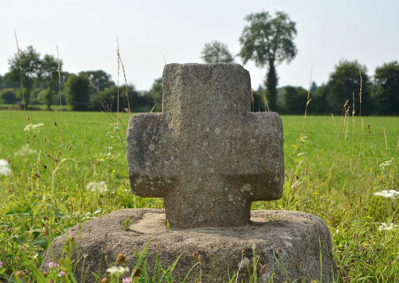 Weathered stone cross monument in a grassy field.