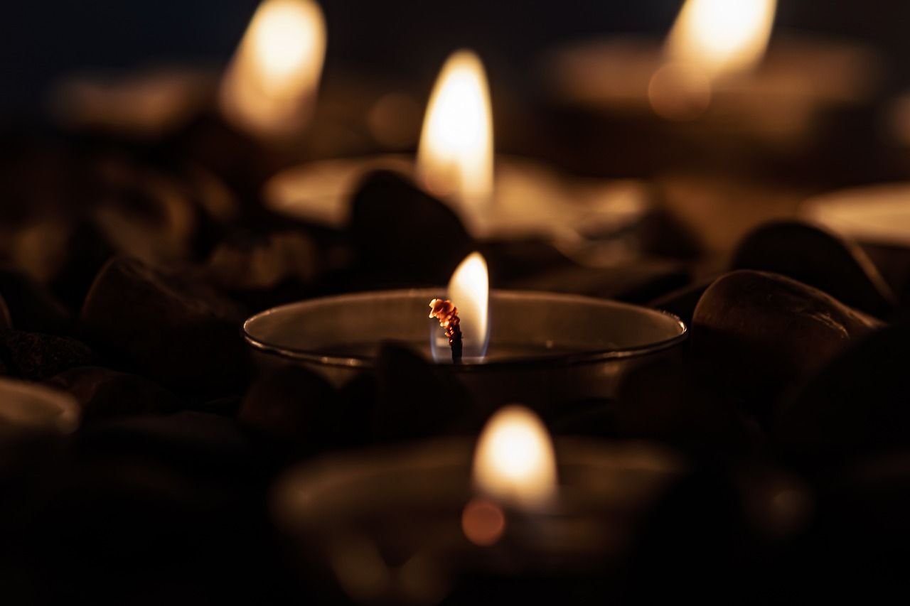 Close-up of a lit tea light candle with a soft glow, surrounded by blurred candles in the background