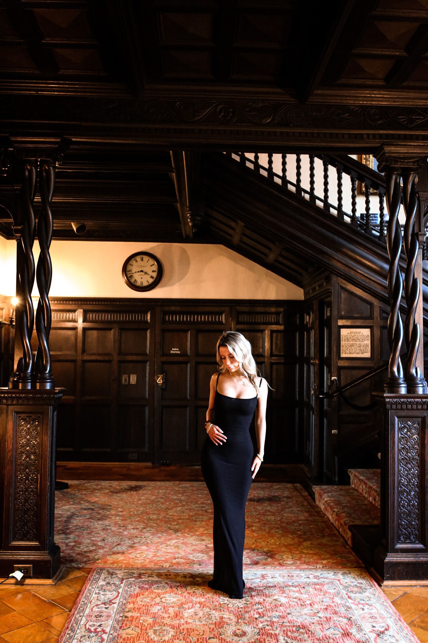 A woman in a black dress is standing in a hallway.