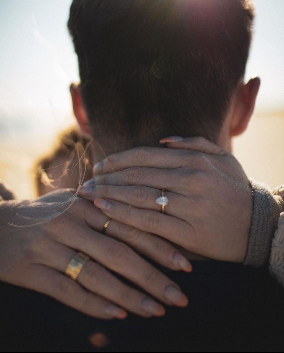 A woman wearing an engagement ring is hugging a man