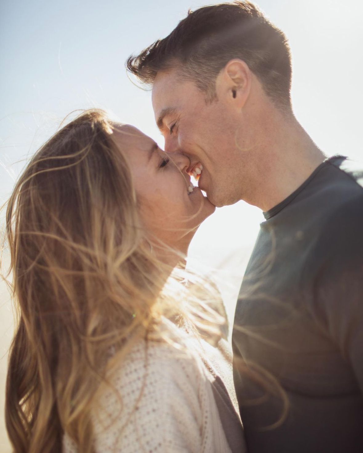 A man and a woman are kissing in front of a blue sky.