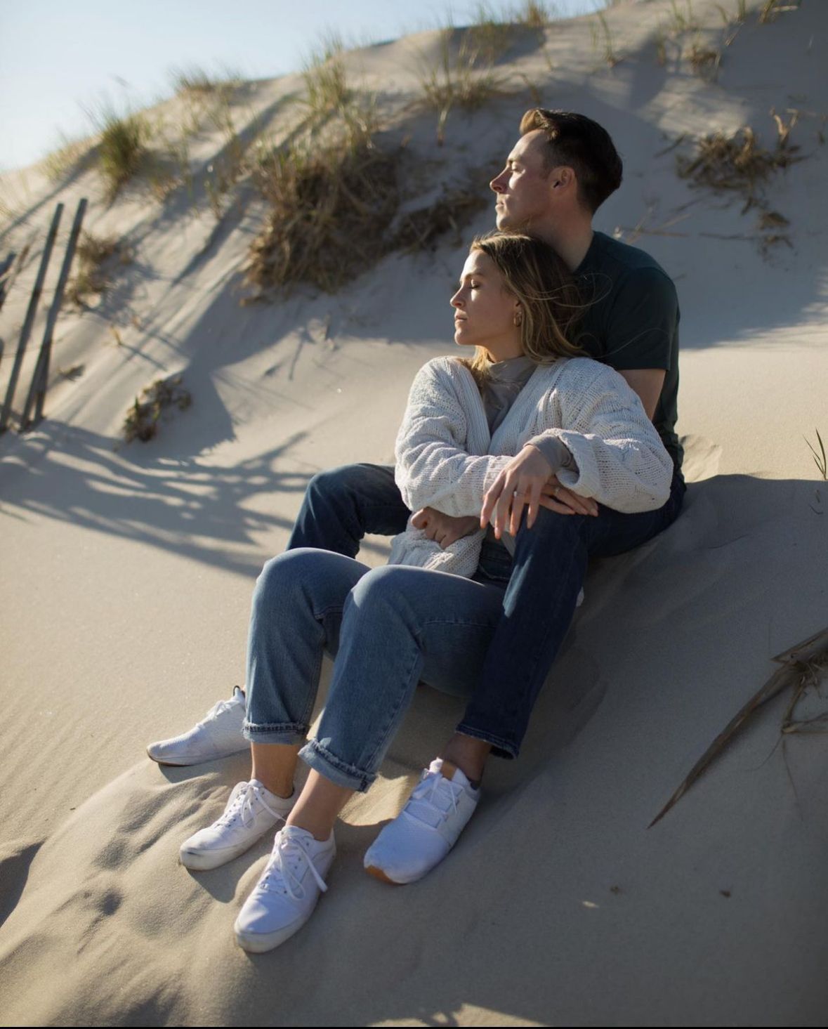 A man and a woman are sitting on top of a sand dune.