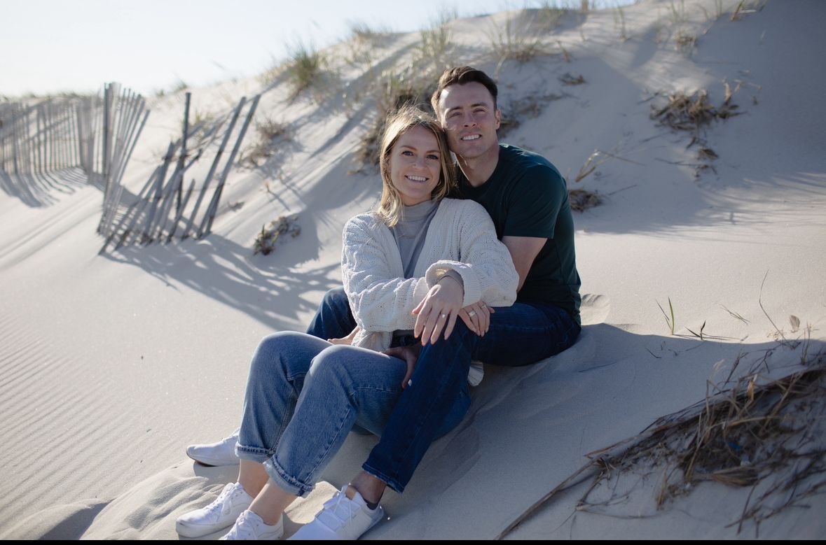 A man and a woman are sitting on top of a sand dune.