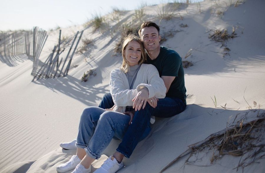 A man and a woman are sitting on top of a sand dune.