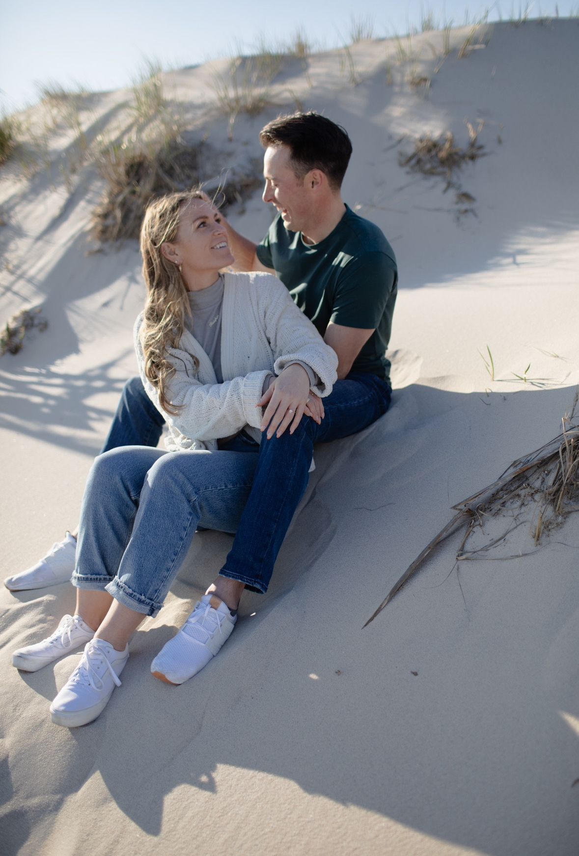 A man and a woman are sitting on top of a sand dune.