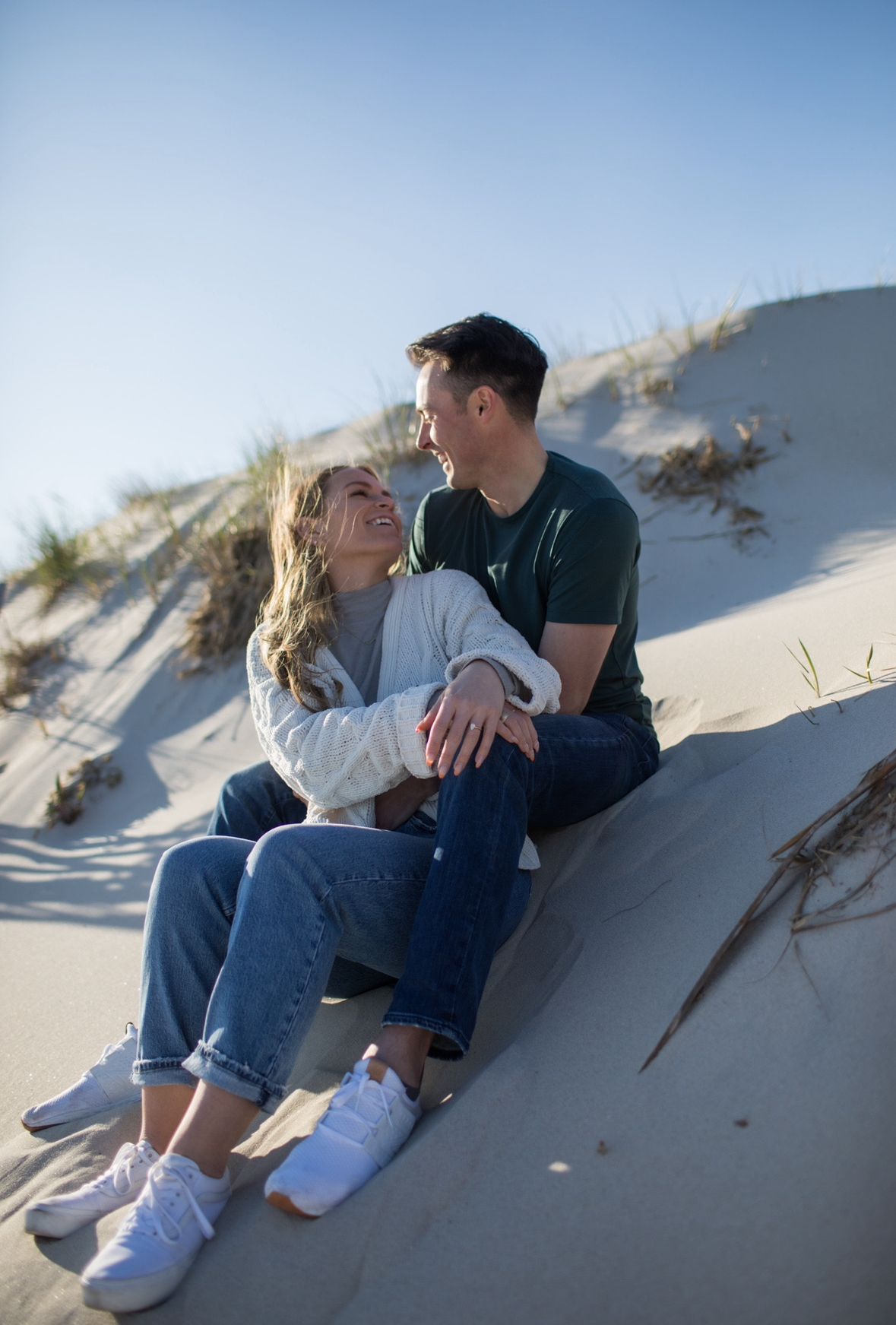 A man and a woman are sitting on top of a sand dune.