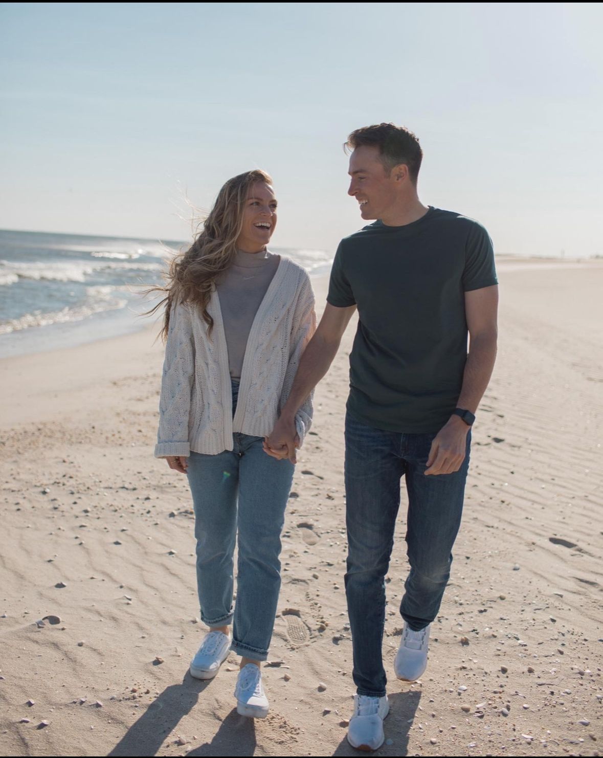 A man and a woman are walking on the beach holding hands.