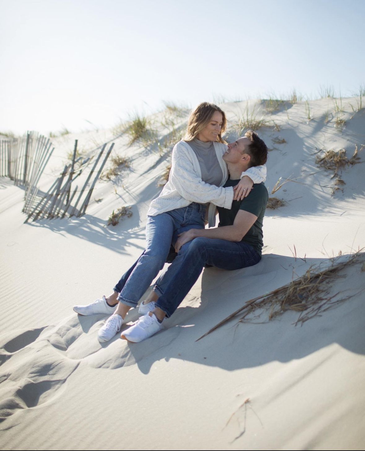 A man and a woman are sitting on top of a sand dune.