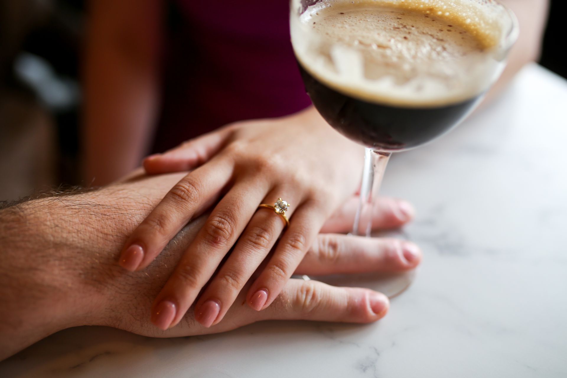 A woman with an engagement ring is holding a man 's hand next to a glass of wine.