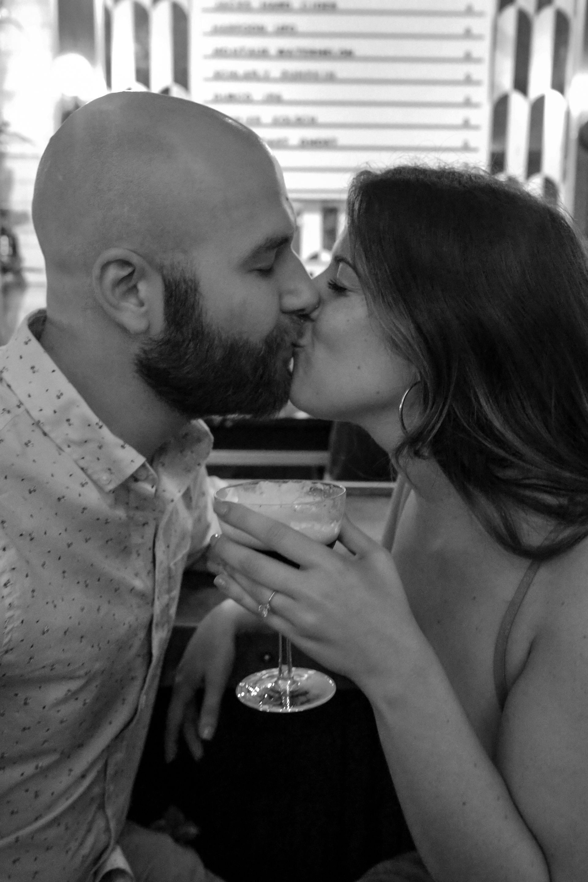 A man and a woman are kissing while holding a glass of wine.