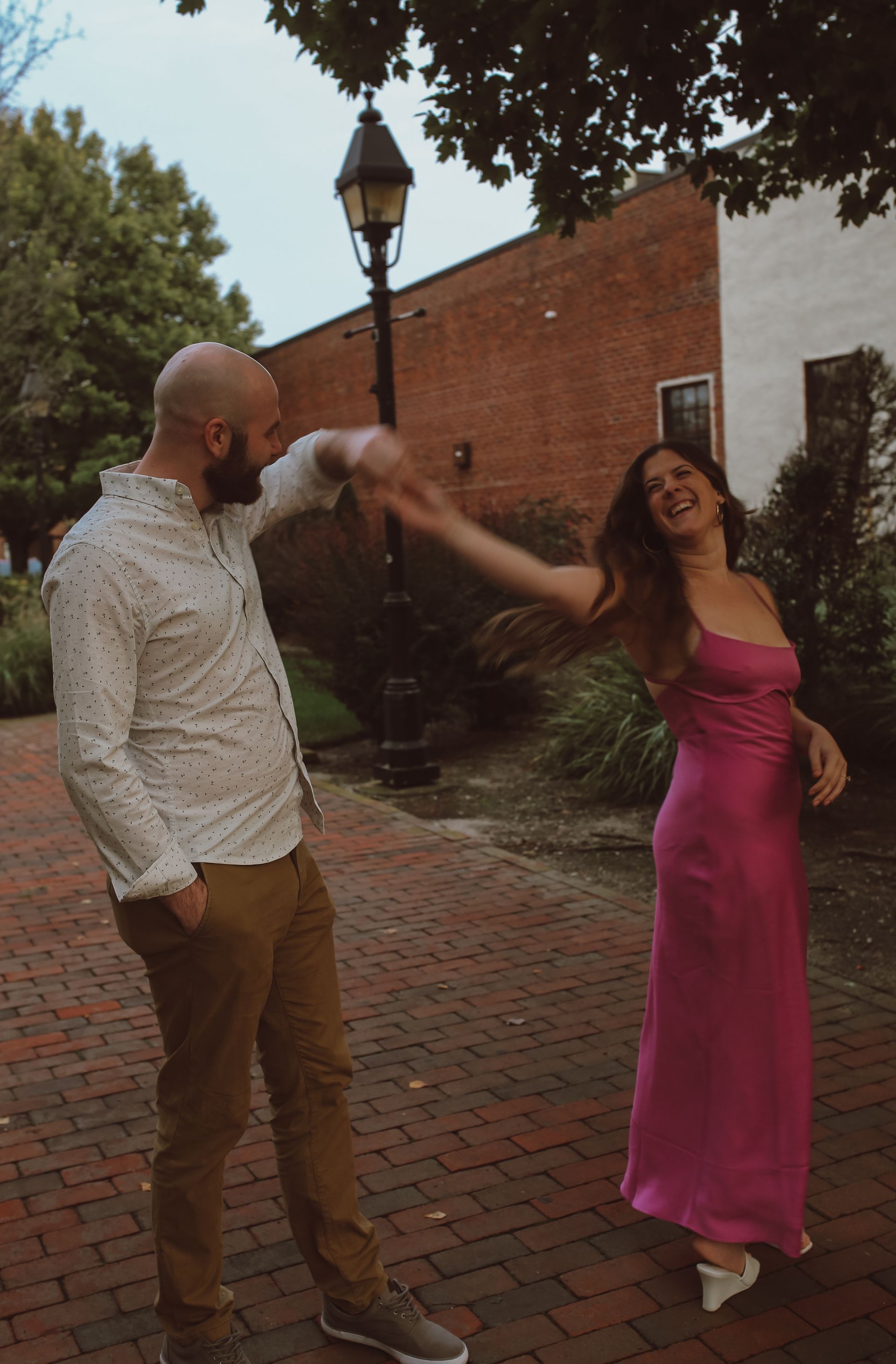 A man and a woman are dancing on a brick sidewalk . the woman is wearing a pink dress.