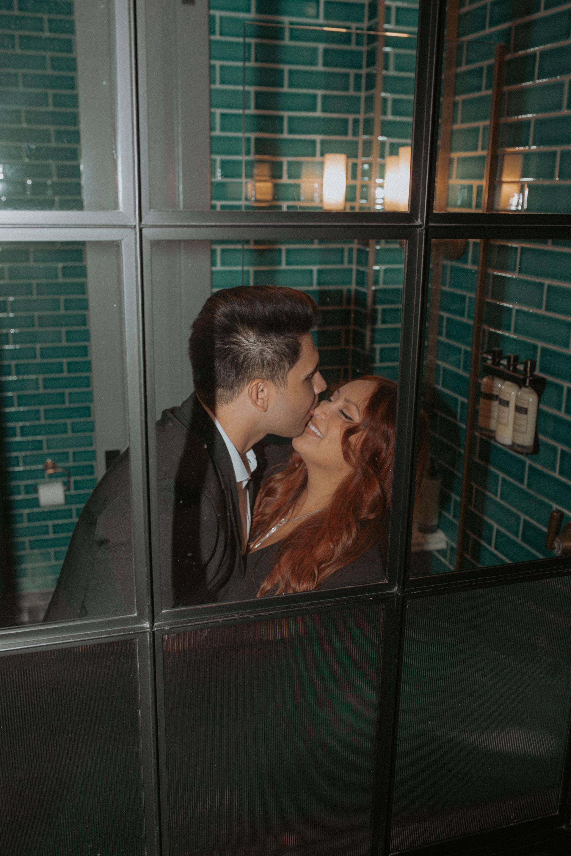 A man and a woman are kissing in a bathroom behind a glass door.