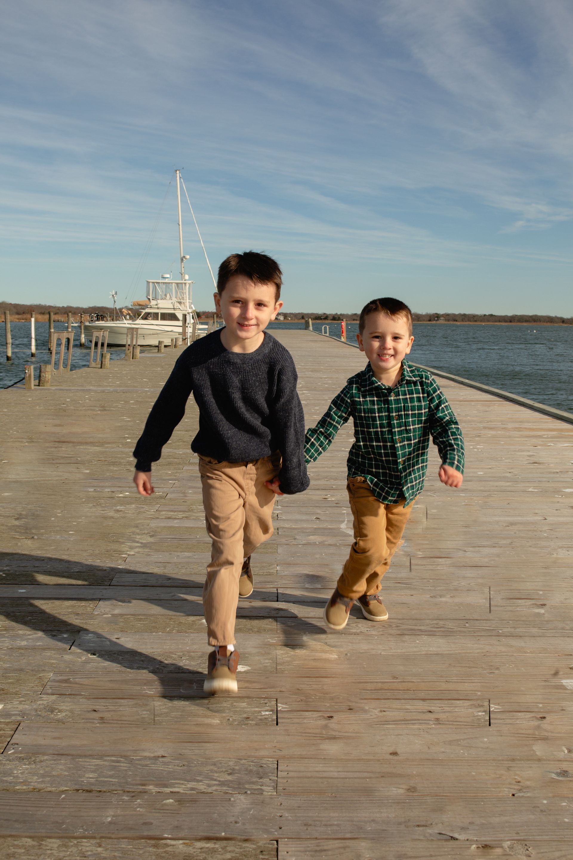 Two young boys are running on a dock holding hands.