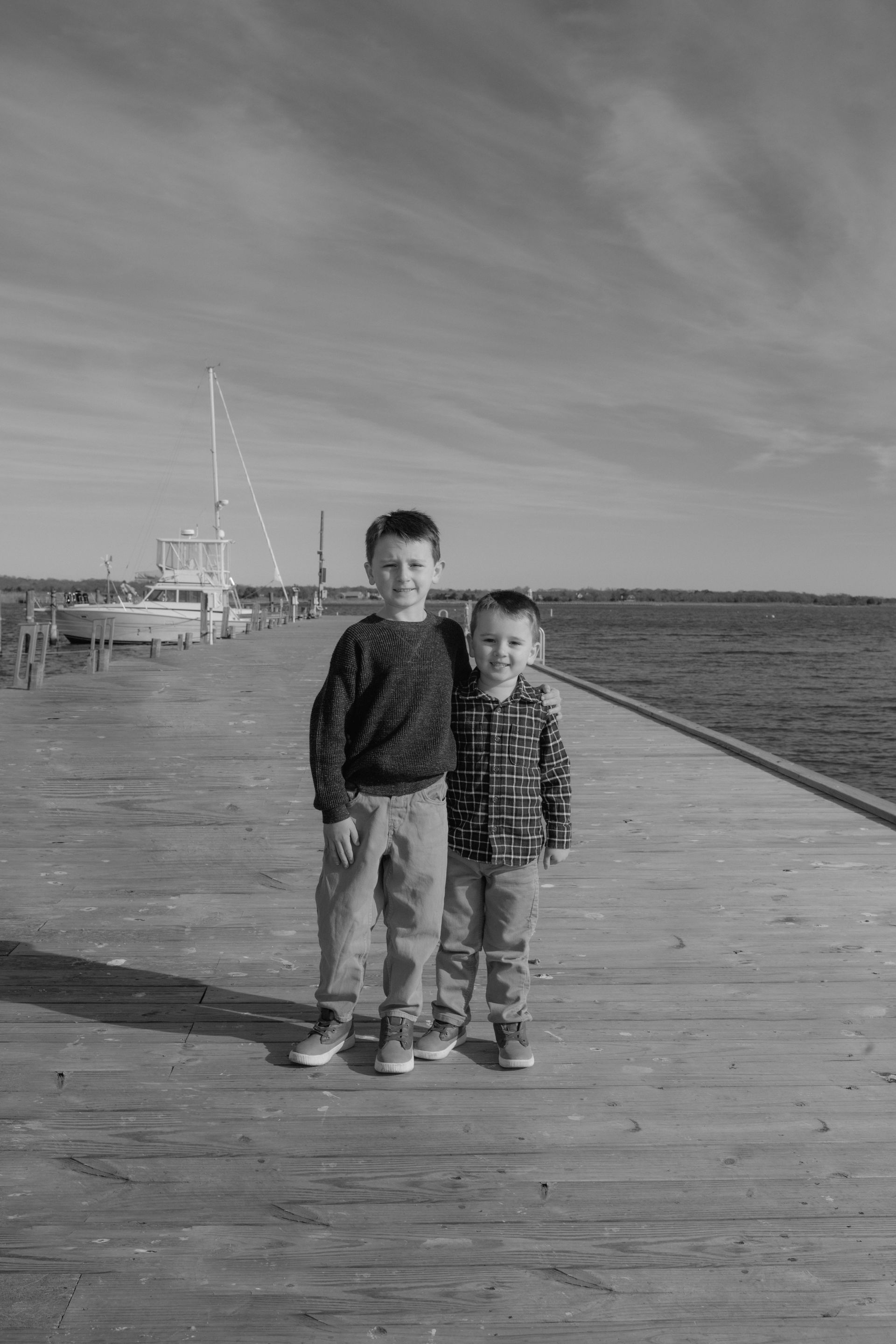 Two young boys are standing next to each other on a pier.