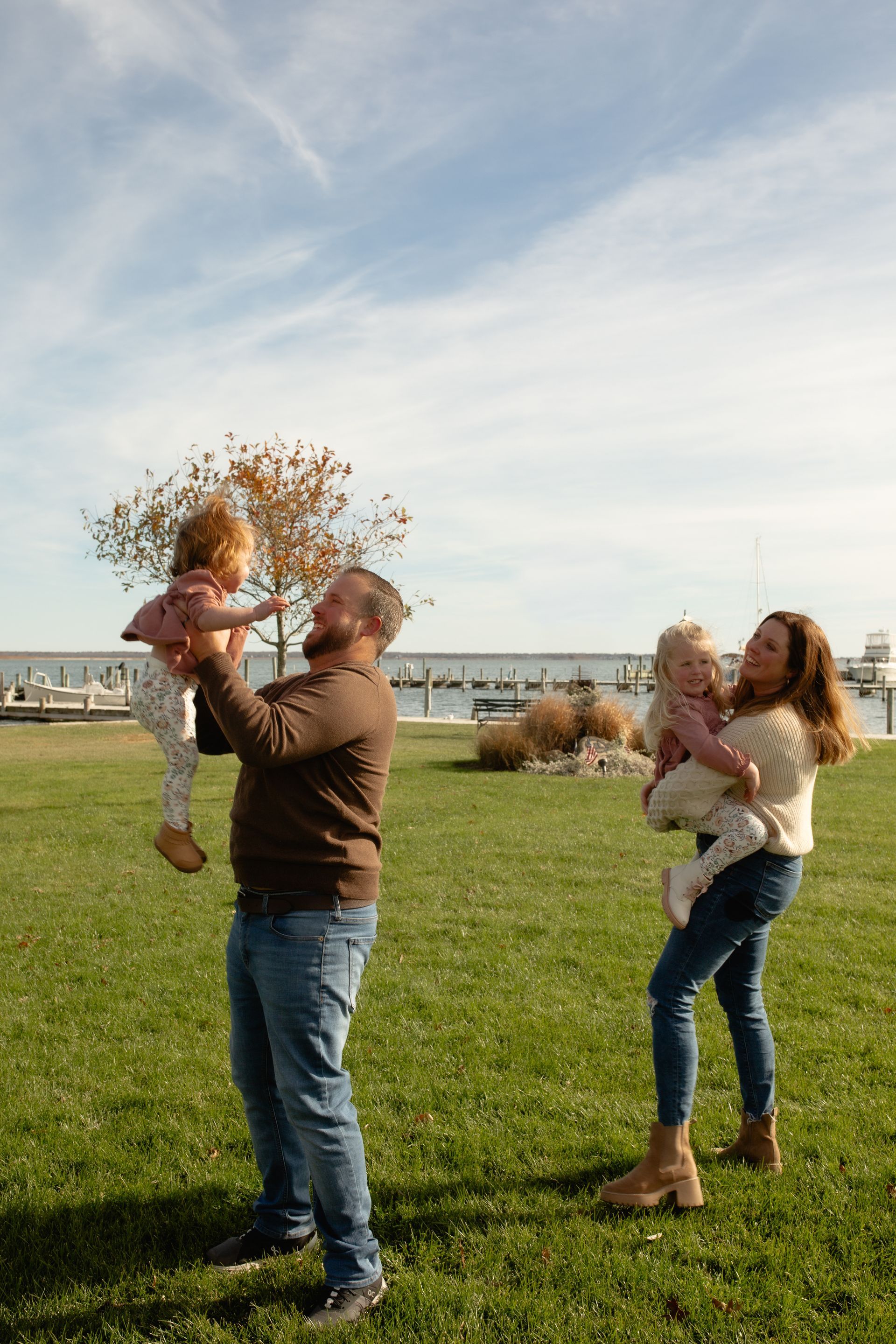 A family is standing in a grassy field holding two children.