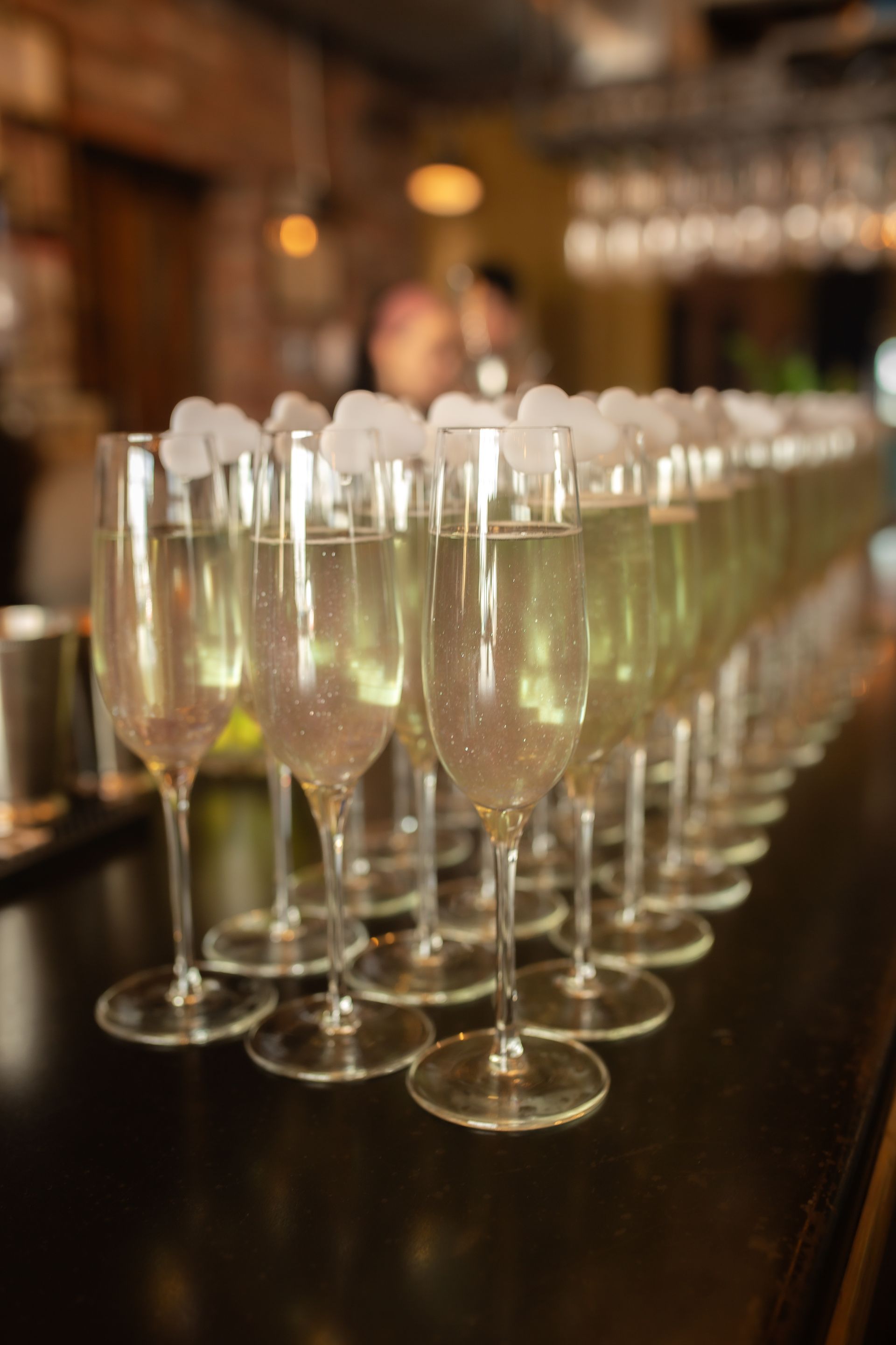 A row of champagne glasses filled with champagne and ice cubes on a bar.