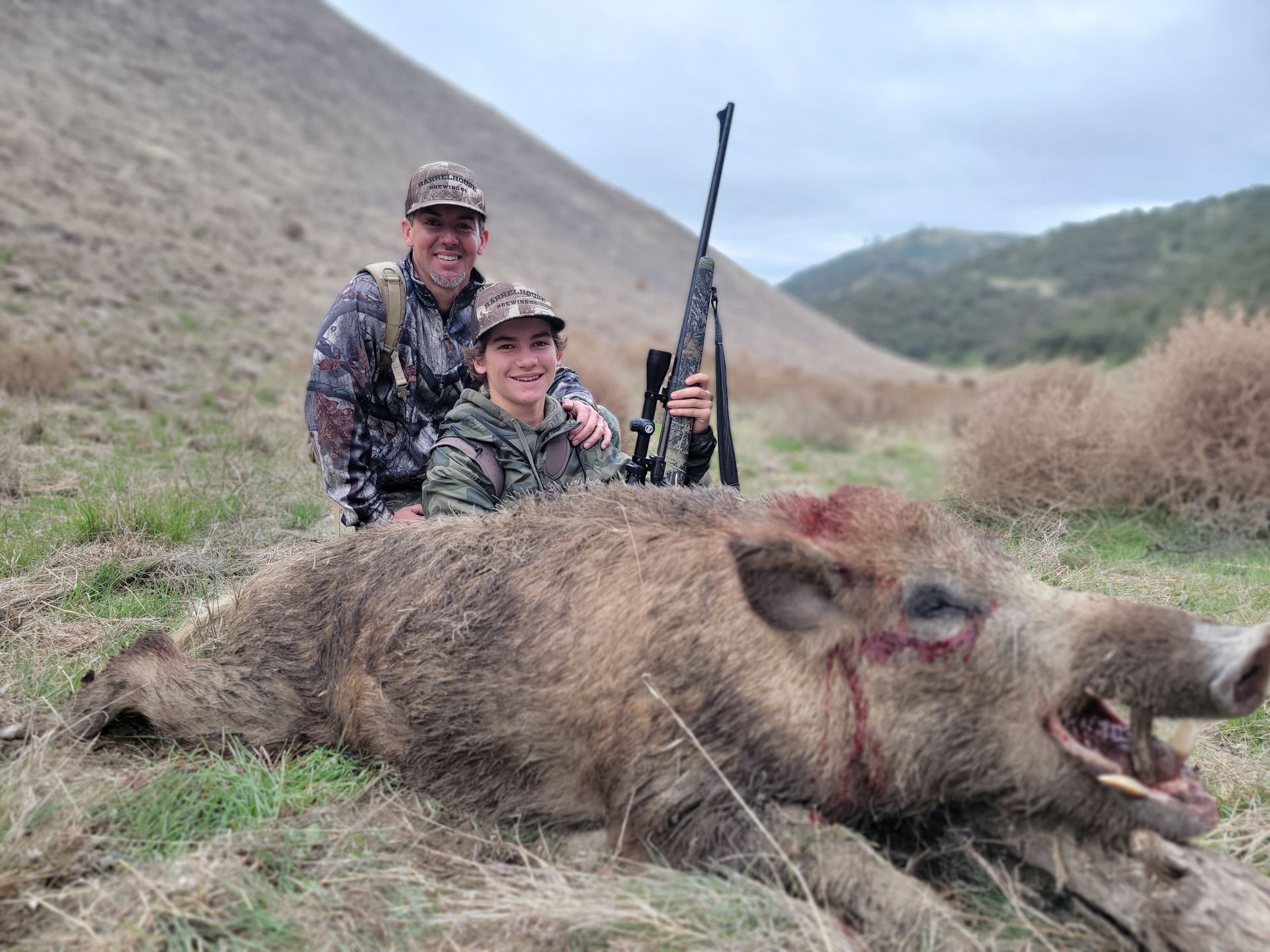 Father and son kneeling behind youth hunters first wild pig taken on guided hog hunt in California