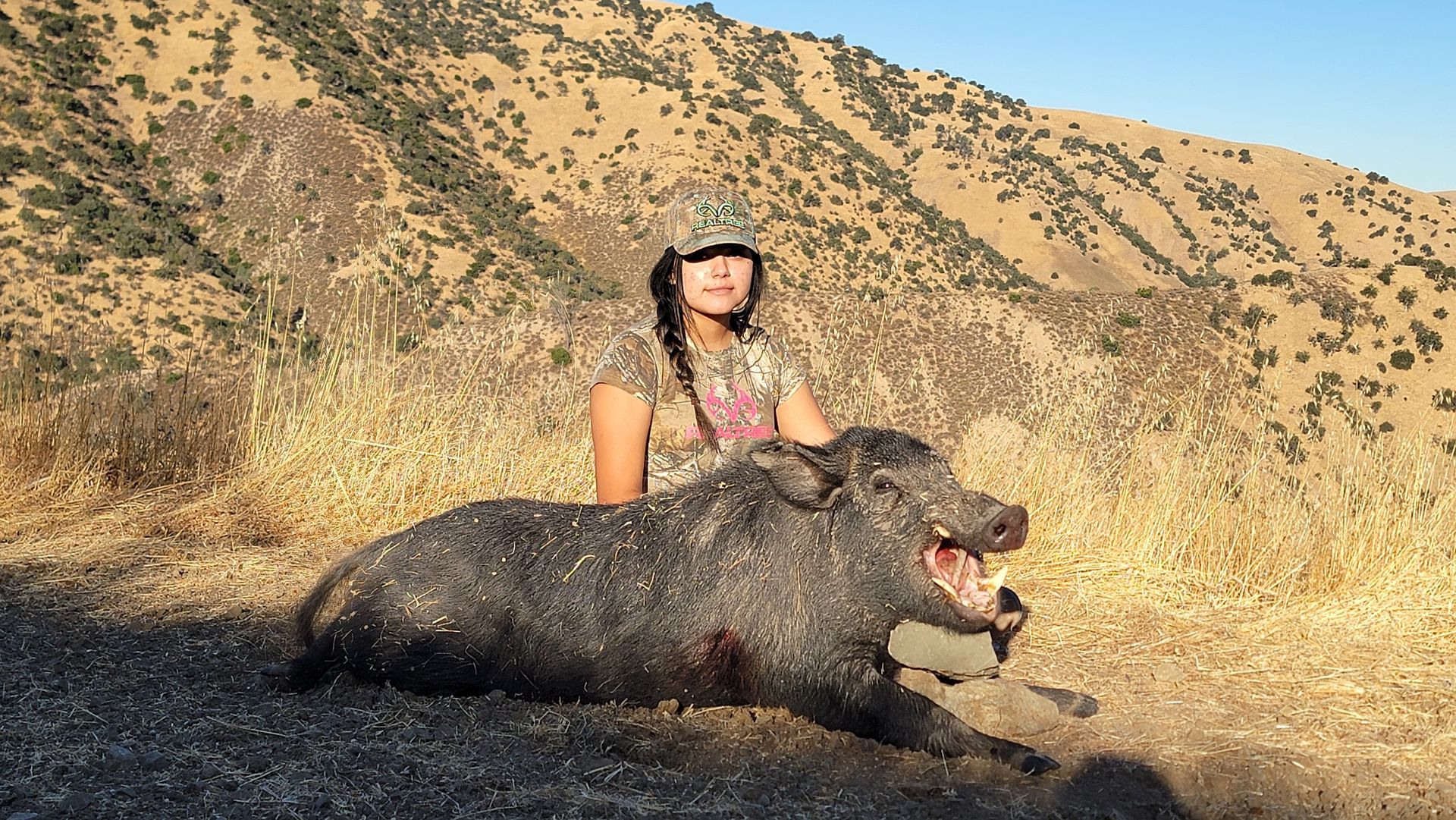 Youth hunter kneeling beside first boar taken on guided pig hunt in California
