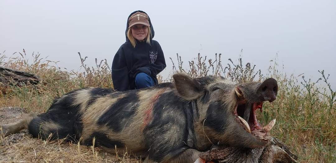 Guide's daughter kneeling beside large trophy wild pig taken on guided pig hunt in California