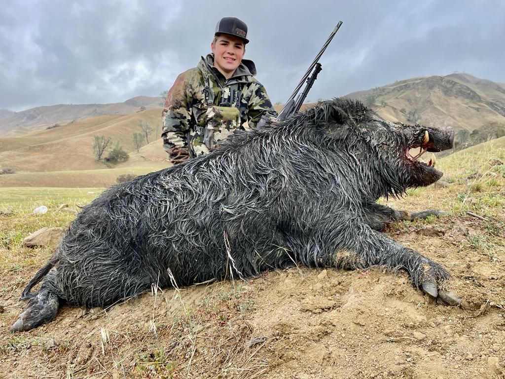 Hunter kneeling beside trophy wild boar taken on guided pig hunt in California