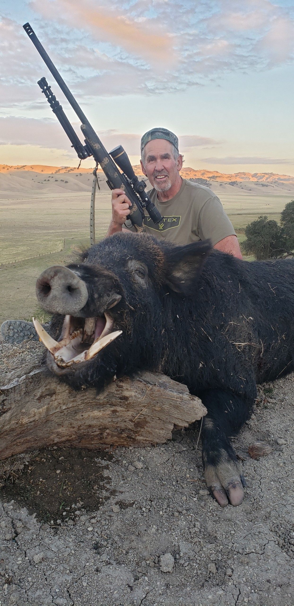 Successful solo hunter kneeling beside massive tusked wild hog