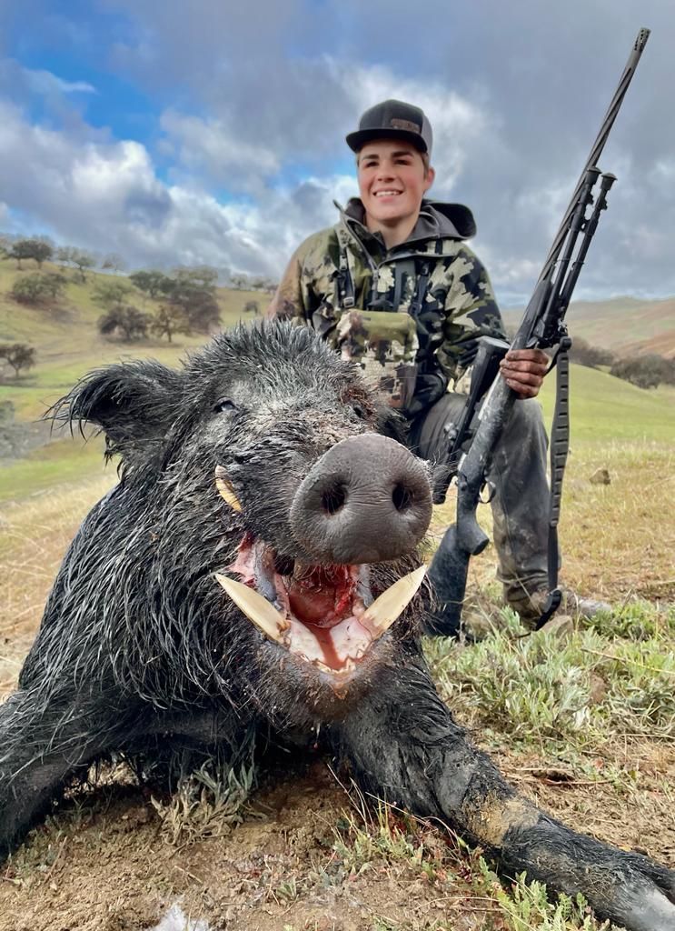 Successful solo hunter kneeling beside massive tusked wild hog