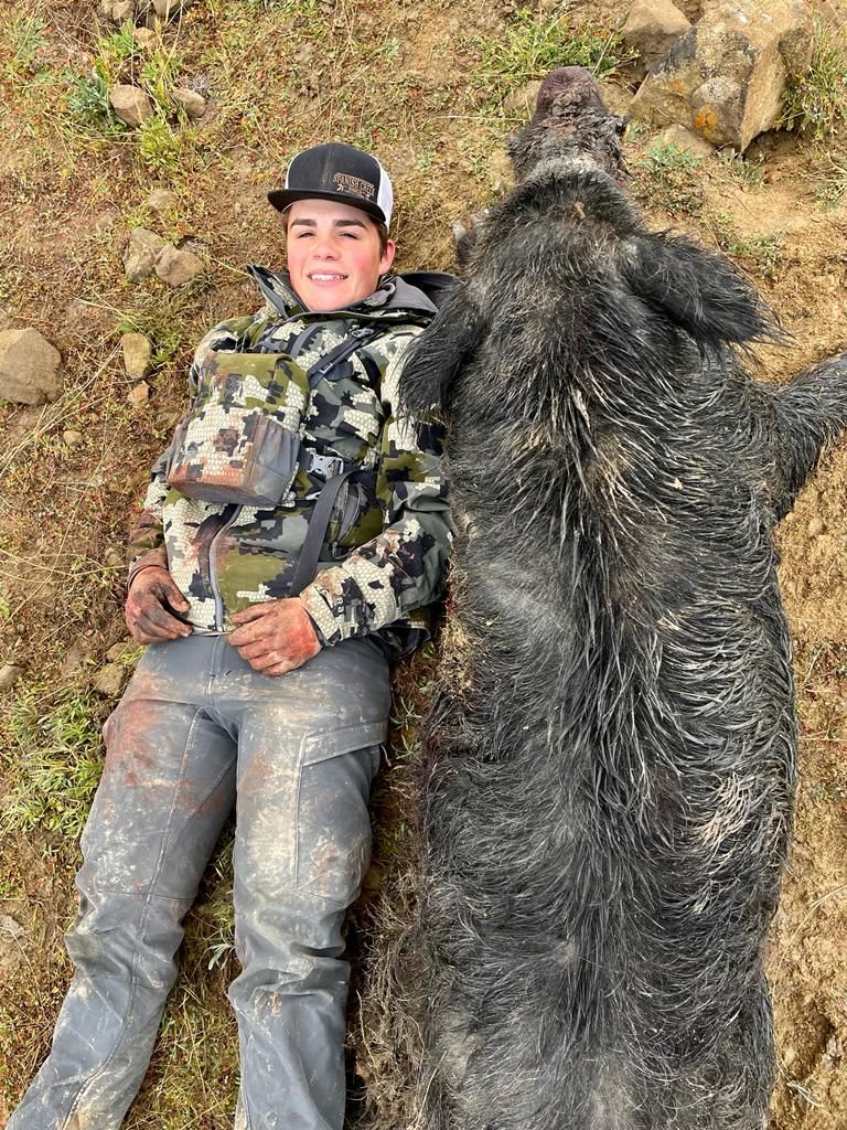Hunter laying beside large wild boar taken on guided pig hunt in California