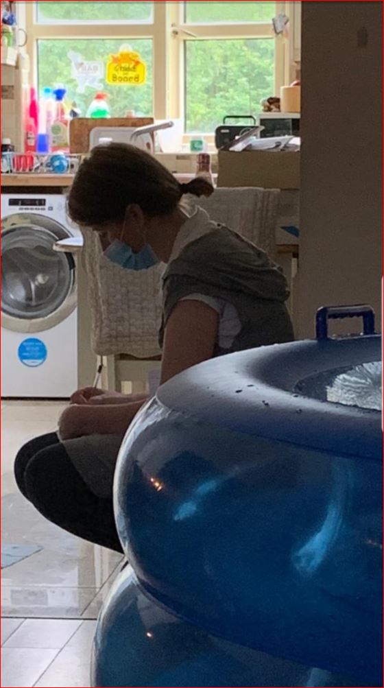 A woman wearing a mask is sitting next to a blue bathtub.