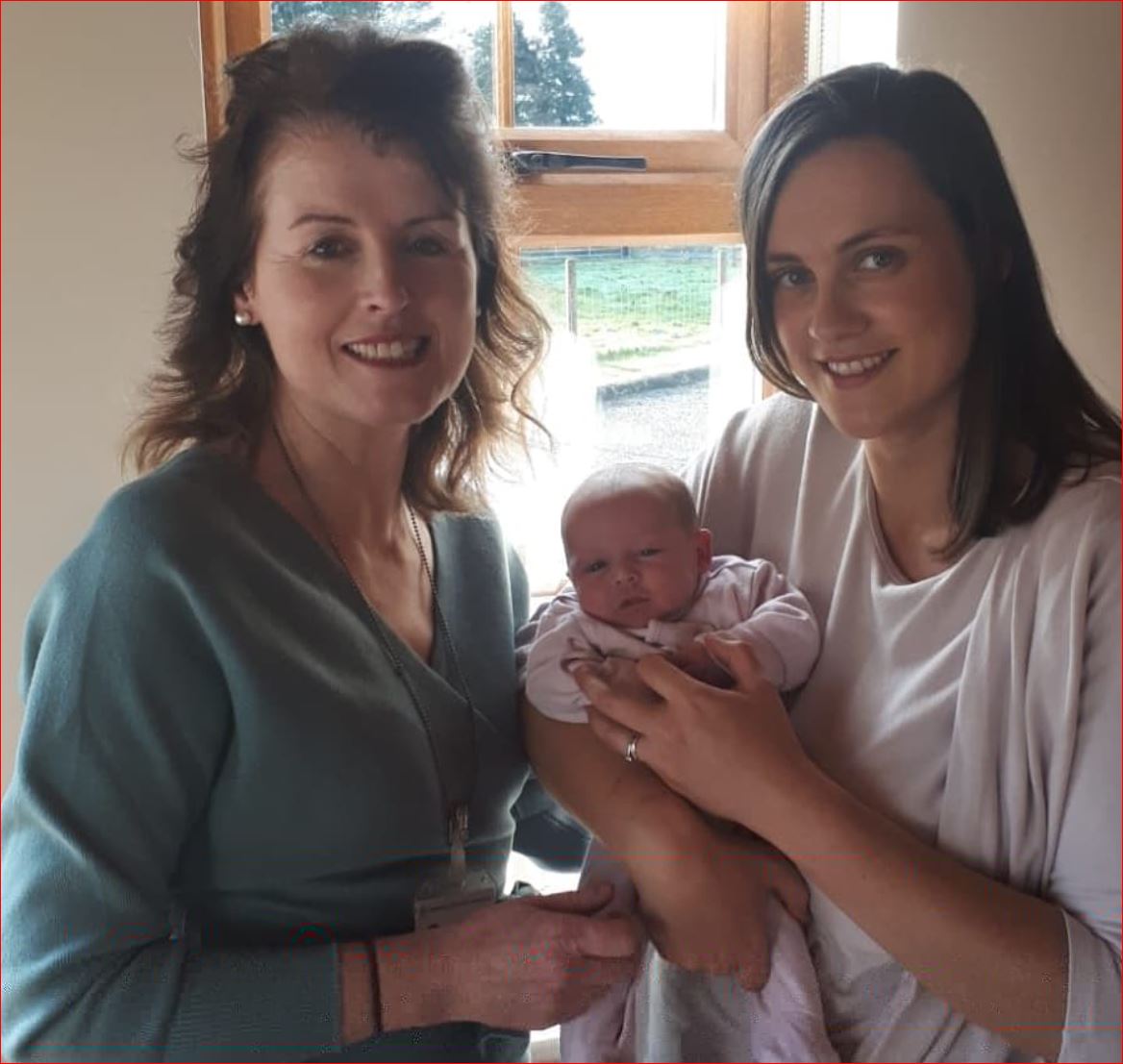 Two women holding a baby in front of a window