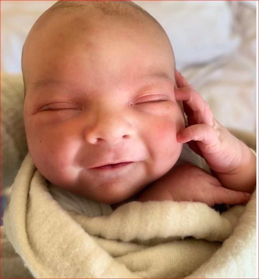 A baby is wrapped in a white blanket and smiling