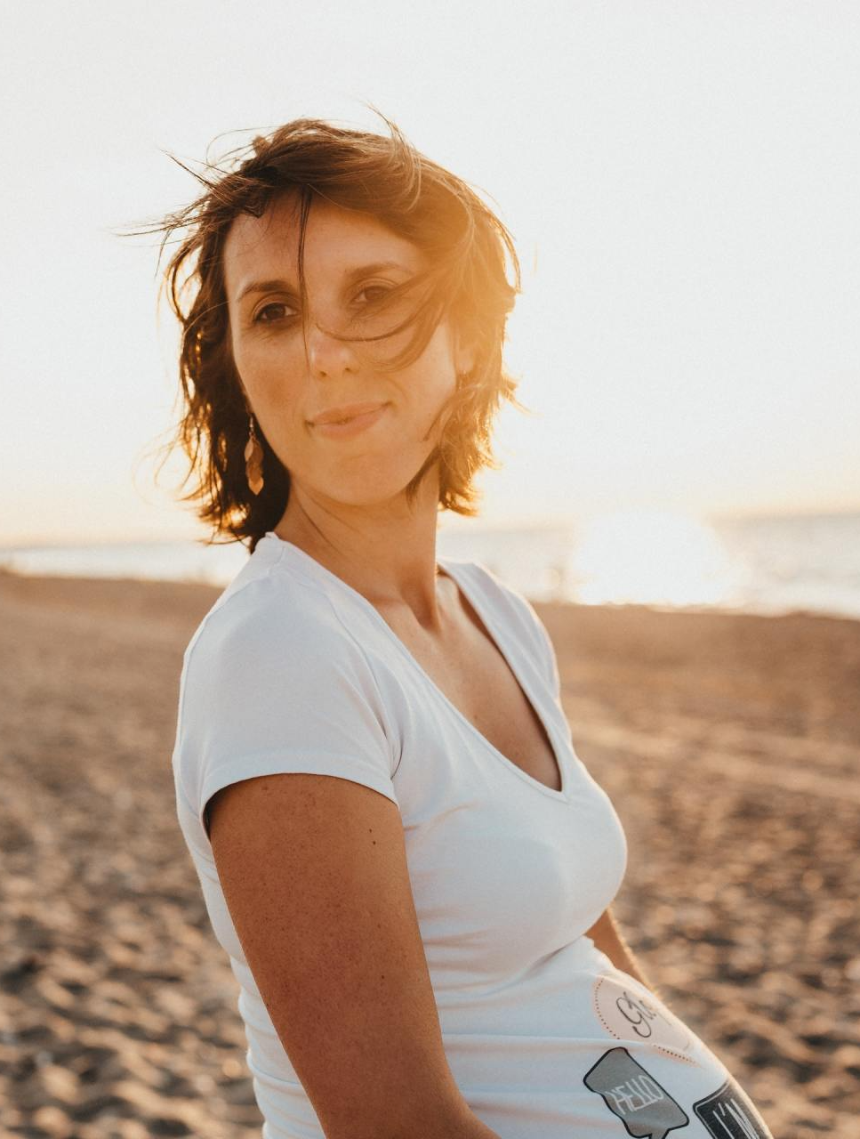 A pregnant woman is standing on the beach at sunset.