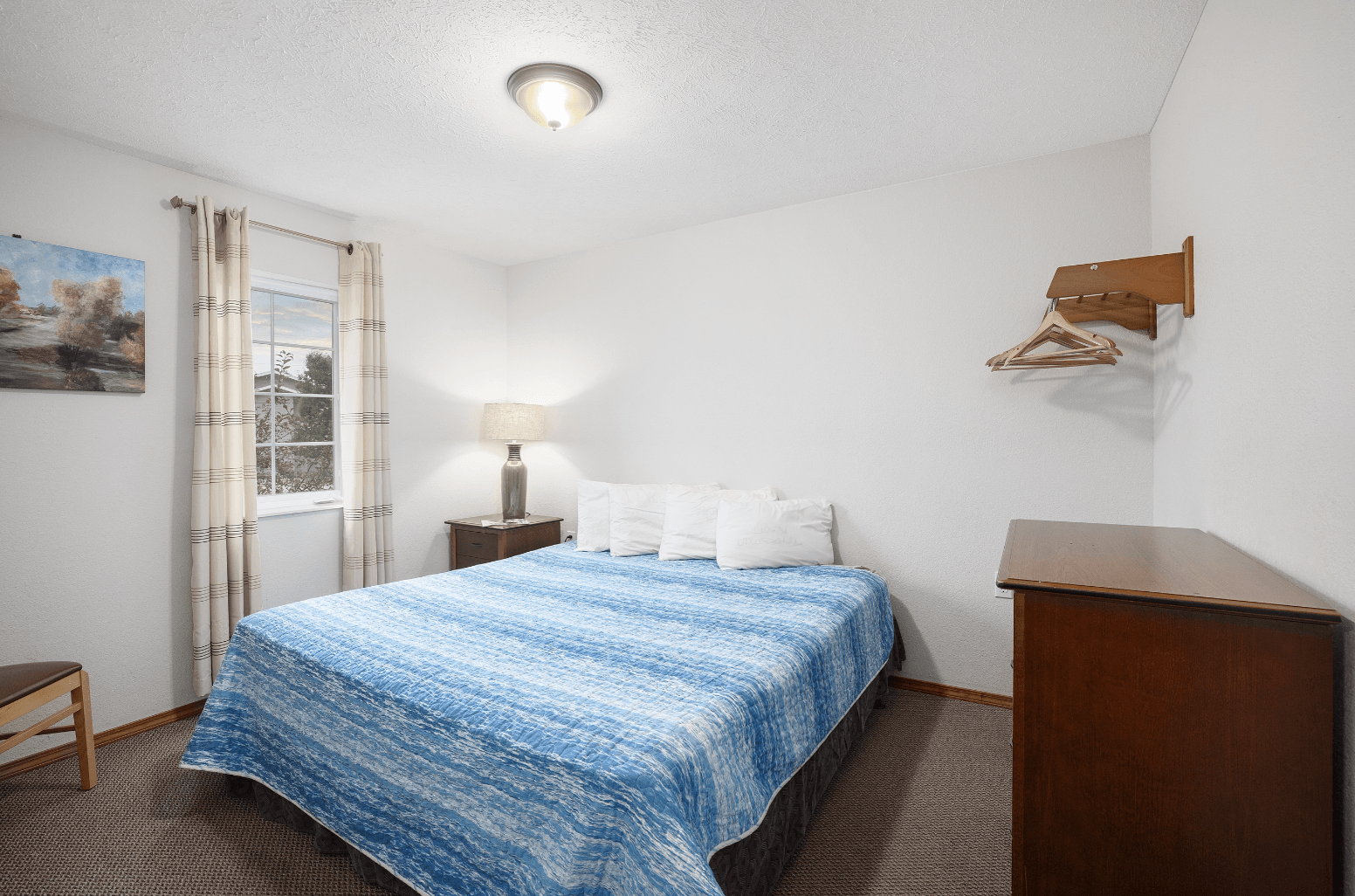 A bedroom with a bed , dresser , lamp and window.