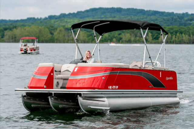 A woman is driving a red pontoon boat on a lake.