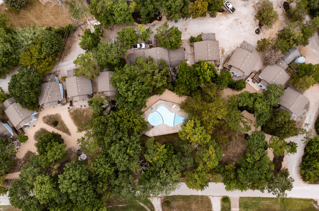 An aerial view of a residential area with houses and a pool surrounded by trees.