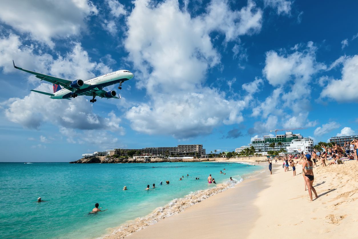 A plane is flying over a beach with people swimming in the water.