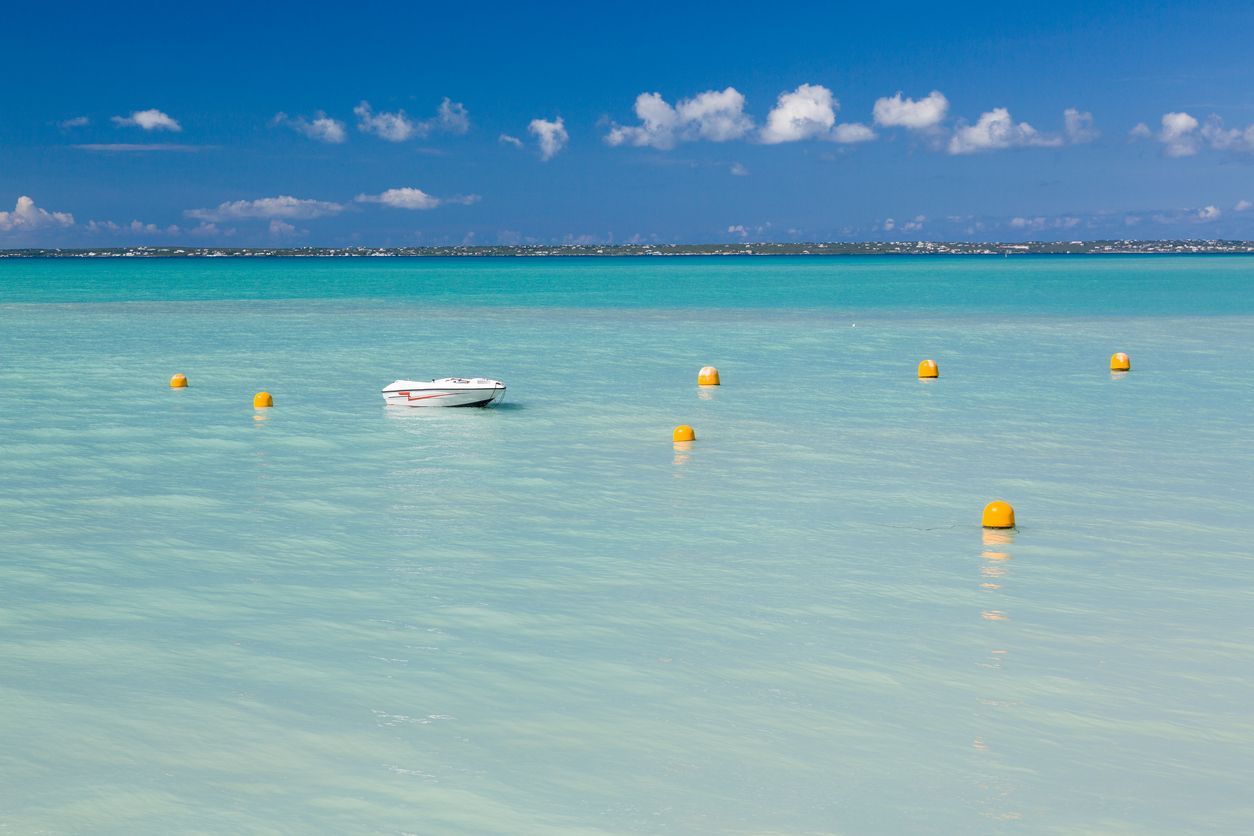 A boat is floating on top of a turquoise ocean surrounded by yellow buoys.